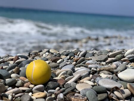 yellow tennis ball on the pebbles beach on sea backgroundの写真素材