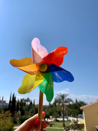 Colorful pinwheel against blue sky in female hand in summer