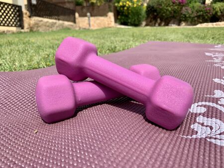 Close-up of pink dumbbells kept on a pink exercise mat in the garden or parkの写真素材