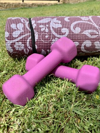 Close-up of pink dumbbells kept near a pink exercise mat in the garden or parkの写真素材