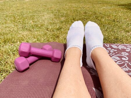 Female legs on the yoga mat with pink dumbbells on the grass in parkの写真素材