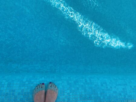 Woman's feet in a swimming pool with blue waterの写真素材