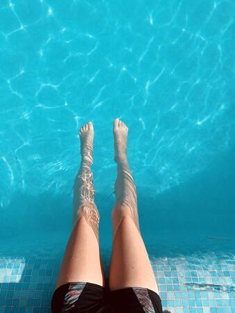 Close-up of a child's legs sitting on a pool of crystal clear blue water. Summer vacation, relax.の写真素材