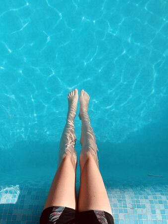 Close-up of a child's legs sitting on a pool of crystal clear blue water. Summer vacation, relax.の写真素材