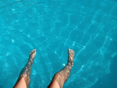 Close-up of a child's legs sitting on a pool of crystal clear blue water. Summer vacation, relax.の写真素材