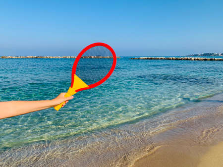 beach tennis racquet in female hand on sandy beachの写真素材