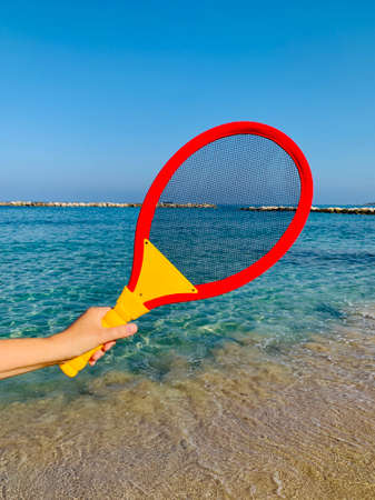 beach tennis racquet in female hand on sandy beachの写真素材