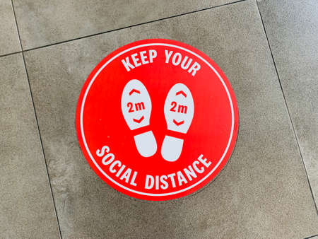 Red round sign printed on ground at supermarket cash desk register informing people to keep 2 meter 6 feet distance from each other,prevent spreadingの写真素材