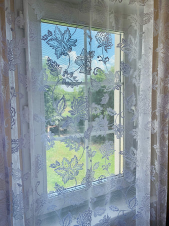 Bright daylight shines through a window draped with white sheer curtains in this semi abstract high key image.の写真素材