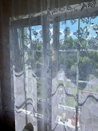 Bright daylight shines through a window draped with white sheer curtains in this semi abstract high key image.の写真素材