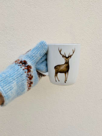 Female hand in mittens holding cup or mug with deer with hot tea or coffee. Tea break. Winter and Christmas time conceptの写真素材