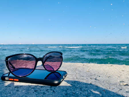 Sunglasses laying on a phone at the beachの写真素材