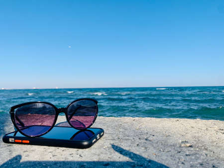 Sunglasses laying on a phone at the beachの写真素材