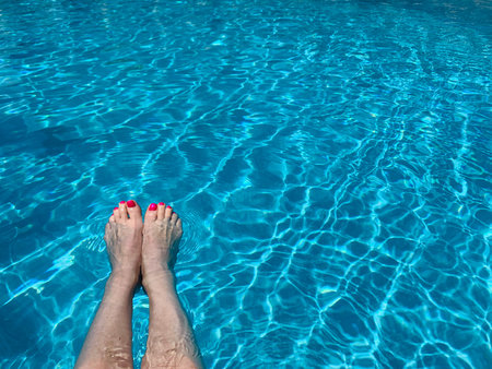 Middle aged woman's legs, with red nail polish on toenails, splashing feet in turquoise blue waters...