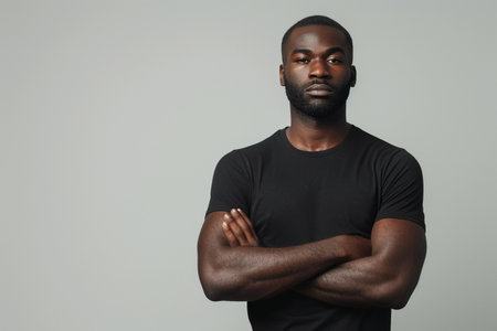 Serious African American Millennial Guy in black t-shirt Crossing Hands Posing Looking At Camera Standing In Studio Over light Background. Shot Of Determined Male. Front View Shotの素材