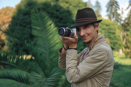 Authentic gray-haired beautiful man in a green hat with a camera on a background of palm trees in the park.の写真素材