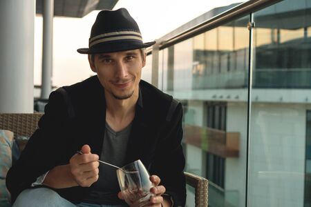 Authentic stylish man in a black jacket and hat eats dessert on the hotel terrace.の写真素材