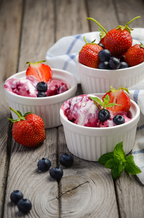 Ice cream with blueberries and strawberries in white bowl on rustic wooden backgroundの写真素材