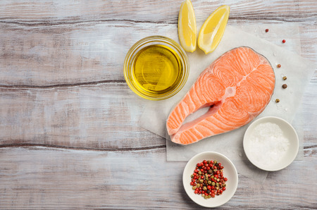 Fresh raw salmon steak with lemon, olive oil and spices on rustic wooden background. Ingredients for making healthy dinner. Healthy diet concept. Top view, copy space.の写真素材