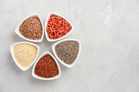 Selection of superfoods in white bowls on gray concrete background. Quinoa, chia, goji berry and flax seeds. Top view, flat lay, copy space.の写真素材