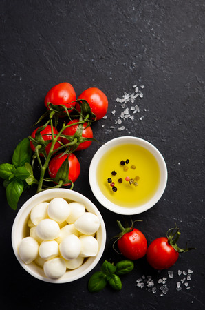 Italian food ingredients - mozzarella, tomatoes, basil and olive oil on black backgroundの写真素材