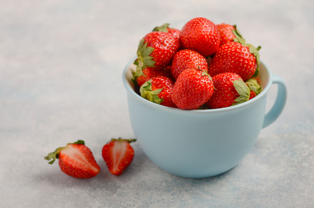Ripe sweet strawberries in blue cup on blue concrete background, selective focus, copy space.の写真素材
