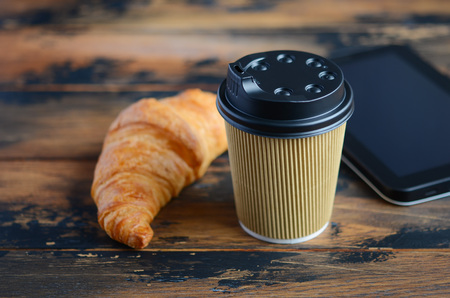 Take away coffee cup with croissant on wooden table.の写真素材