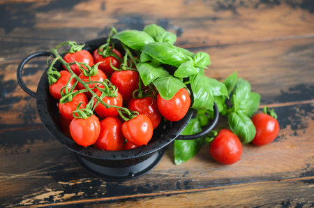 Cherry tomatoes and basil in a colander on a wooden backgroundの写真素材