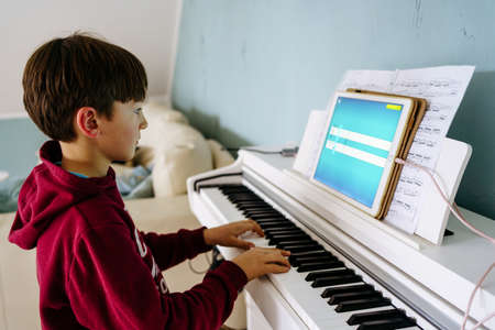 Boy playing digital piano at home with deviceの写真素材