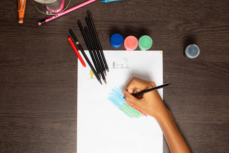 Child's hand drawing with crayons on white sheet of paper
