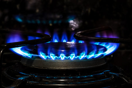 Gas burner with blue flame, glowing fire ring on kitchen stove.