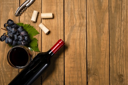 Bottle cup and bunch of grape and vine leaf on wooden background. Top view with copy space.の写真素材