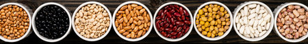 Assortment of beans in a pot. Wooden black background.