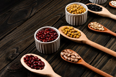 Diversity of beans inside wooden spoons. Black wood background.