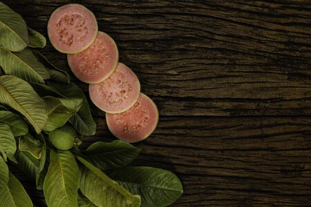 Fresh red guavas with green leaves on wooden demolition background. Wood texture and guava leaves.の写真素材