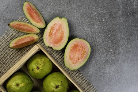 Wooden box with red guavas on concrete background. Concrete texture. Cut pieces of guava.の写真素材