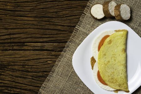 Crepioca. Pancake of cassava (tapioca) with cheese and tomato on plate on old wooden background. Selective focus.の写真素材
