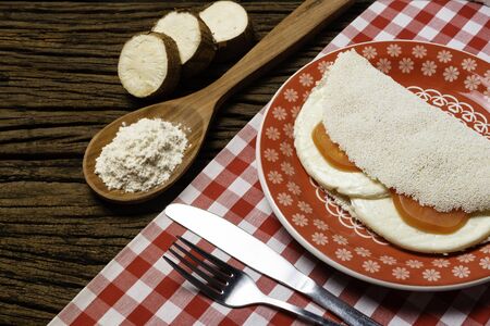 Casabe (bammy, beiju, bob, biju). Flatbread of cassava (tapioca) with caprese salad (tomato, mozzarella) on plate old wooden background. Selective focus.の写真素材