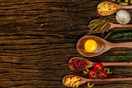 Different pasta types in wooden spoons on the table. Top view. Space for text. Old wooden background.の写真素材