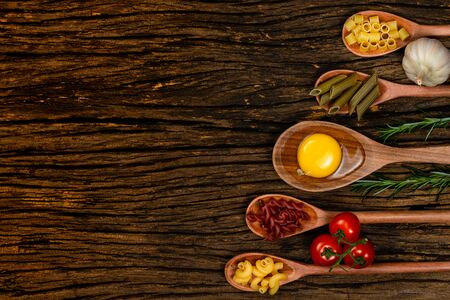 Different pasta types in wooden spoons on the table. Top view. Space for text. Old wooden background.の写真素材
