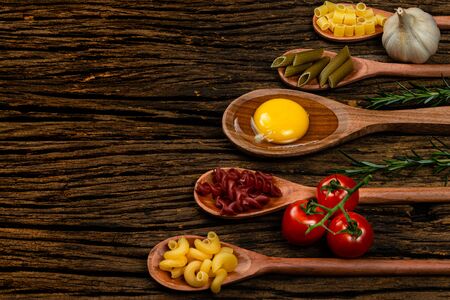 Different pasta types in wooden spoons on the table. Top view. Space for text. Old wooden background.の写真素材