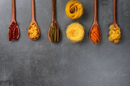 Different pasta types in wooden spoons on the table. Top view.の写真素材