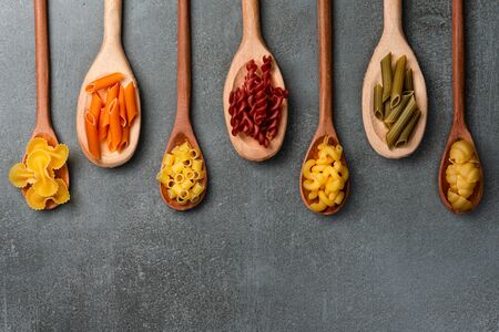 Different pasta types in wooden spoons on the table. Top view.の写真素材