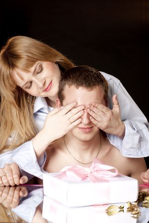 Happy woman covering her husband's eyes to surprise him with a giftの写真素材