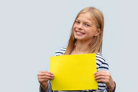 smiling girl holds a blank yellow sheet of paper. Isolated on a gray backgroundの写真素材