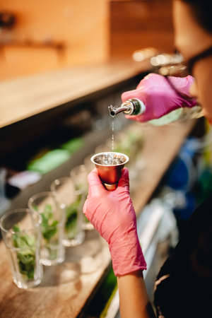 The girl prepares a mojito cocktail. Pours rum in measuring cup. Blurred background. Vertical frameの写真素材