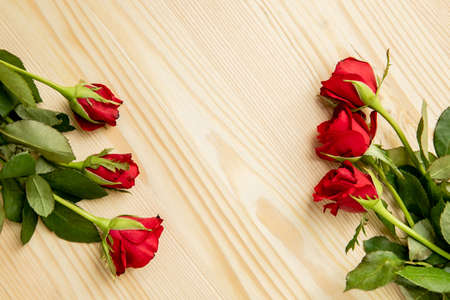 Red roses lie on a wooden table, frame decorated with flowers. There is a place for text. Postcard to the day of lovers, March 8.の写真素材