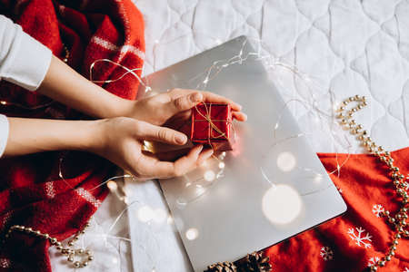 Womans hands holding gift decorated with a garland on the background of a laptop. Flat lay composition for christmas.の写真素材