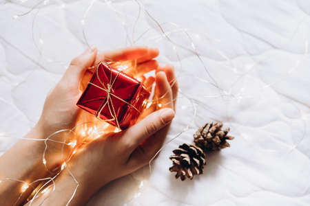 Womans hands holding red gift box decorated with a garland on the white background. top view. Flat lay composition for Christmas.の写真素材