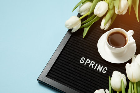 Cup of coffee and white tulips on a felt board with the inscription in English spring.の写真素材
